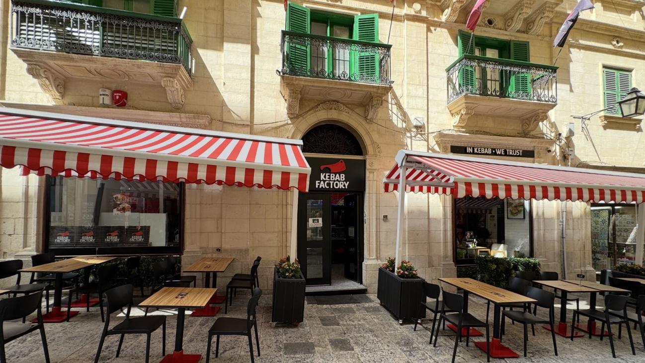 Kebab Factory restaurant storefront with red-and-white striped awnings on a historic Maltese street, tables set outside for lunch
