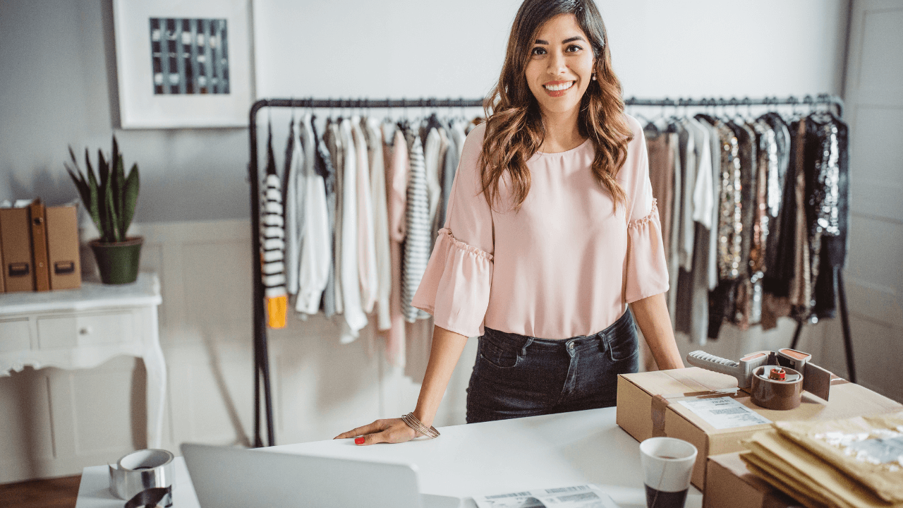 A female entrepreneur standing at a desk, with a rail of clothes behind her. 