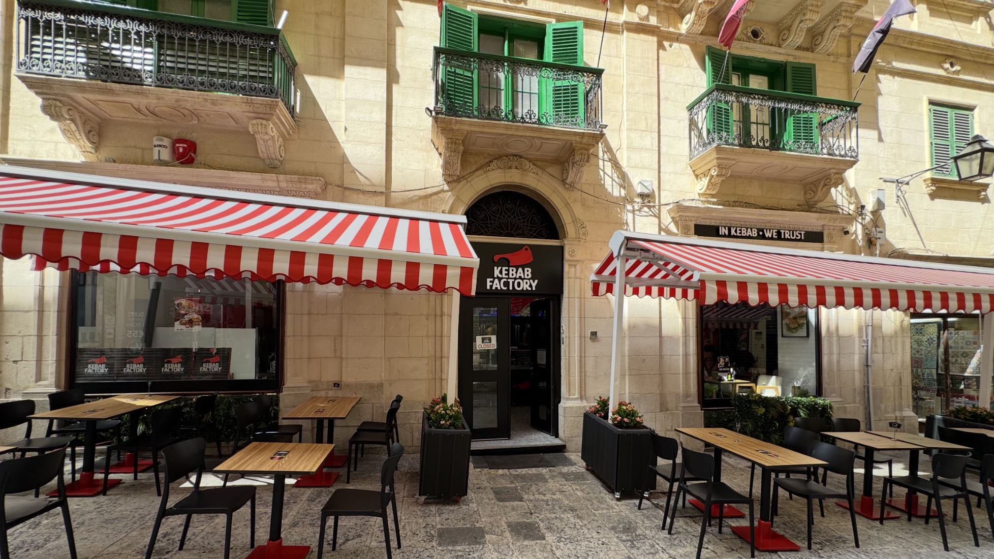 Kebab Factory restaurant storefront with red-and-white striped awnings on a historic Maltese street, tables set outside for lunch